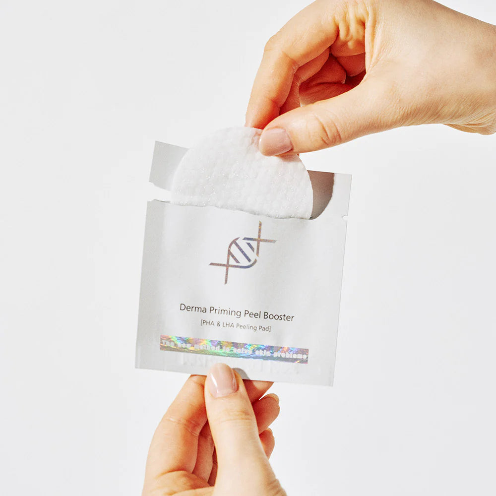 Hand holding a Derma Priming Peel Booster package against a white background